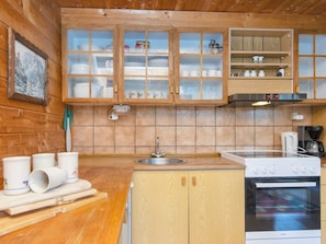 A wooden cabin kitchen with a sink, stove, and cabinets.