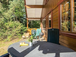 Une cabane en bois dotée d’un patio couvert, d’une table garnie de fruits et de sièges d’extérieur.