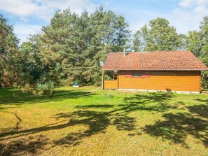 A single-story wooden cabin with a tiled roof, surrounded by a grassy yard and dense trees. - 6 Person Holiday Home in Orsted (Ørsted)