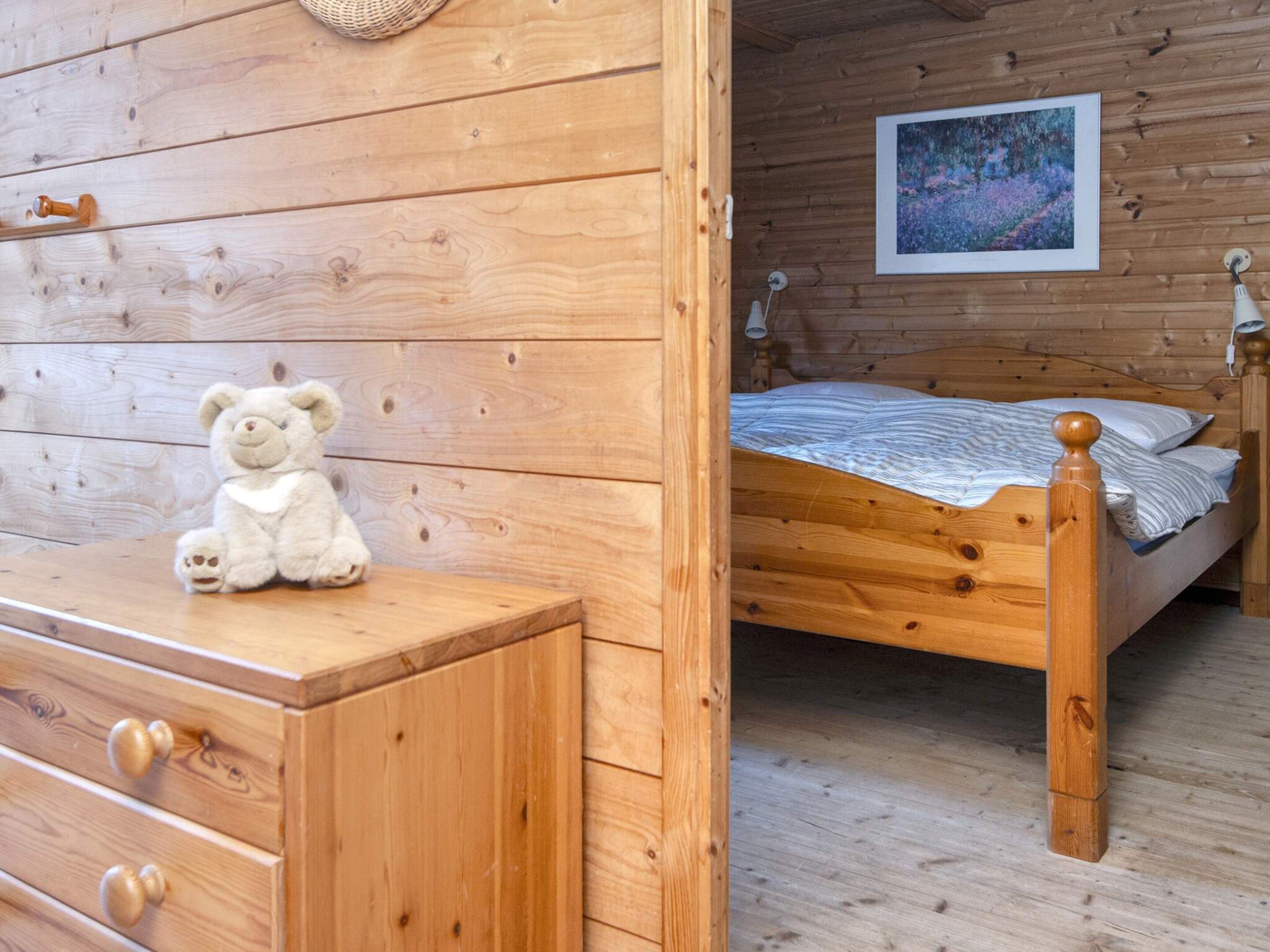 Una habitación con piso de madera, una cama, un tocador y un oso de peluche.