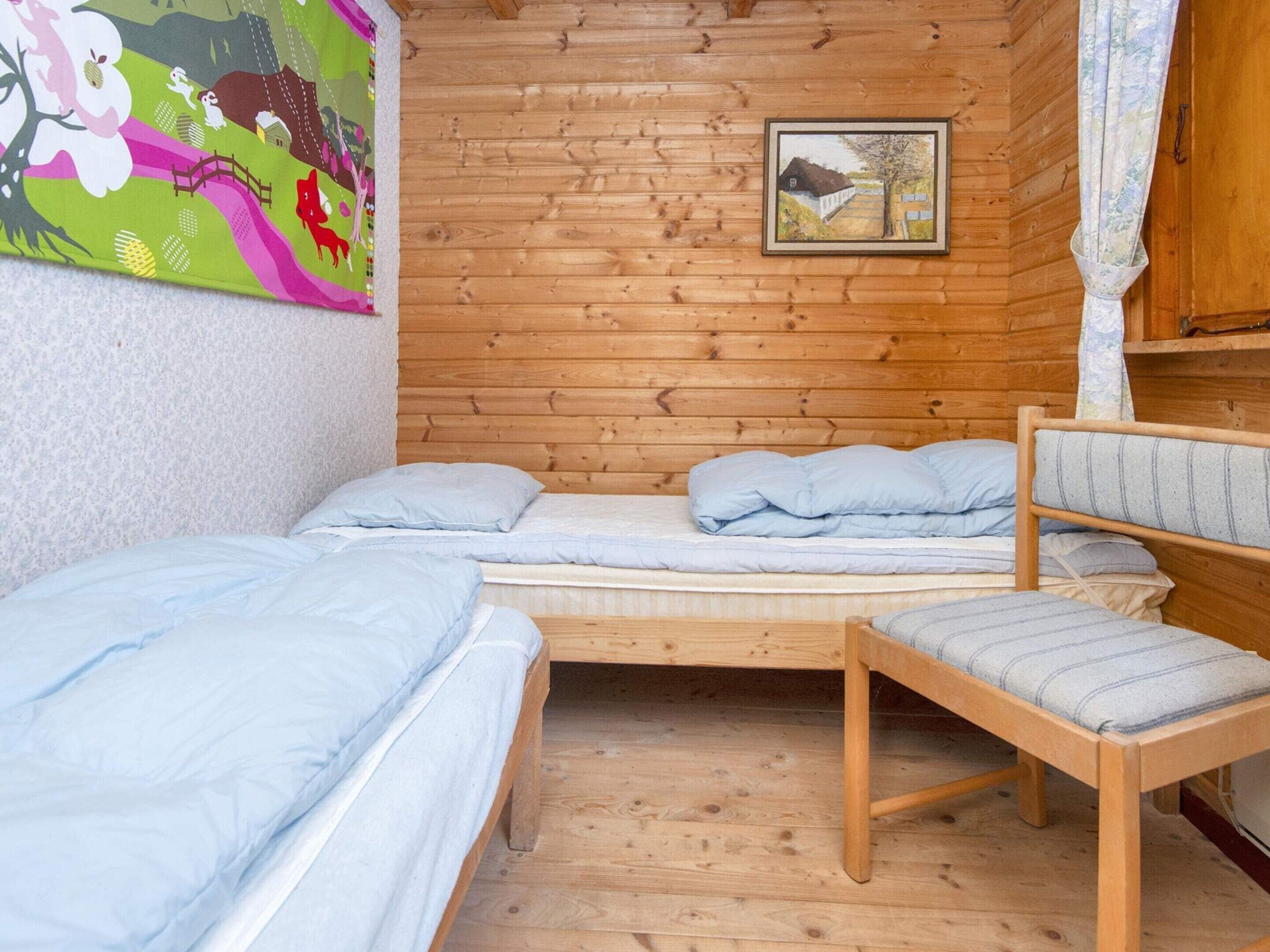 Uma cabana com interior em madeira, uma cama com roupa de cama azul, uma cadeira e um quadro na parede.