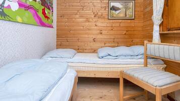 Uma cabana com interior em madeira, uma cama com roupa de cama azul, uma cadeira e um quadro na parede.
