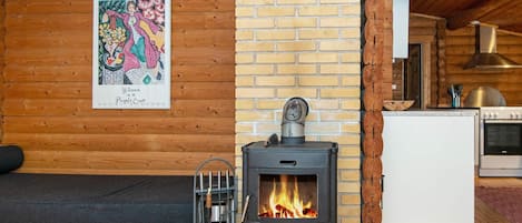 A cozy cabin interior with a wood-burning stove, a sofa, and a kitchen area.