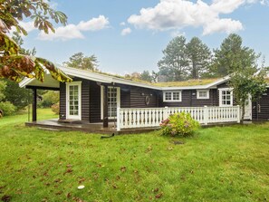 A log cabin with a porch, a fenced yard, and a grassy lawn.