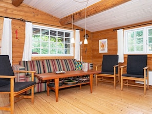 A cozy cabin interior with a wooden floor, a striped sofa, a table with a bowl, and two chairs.