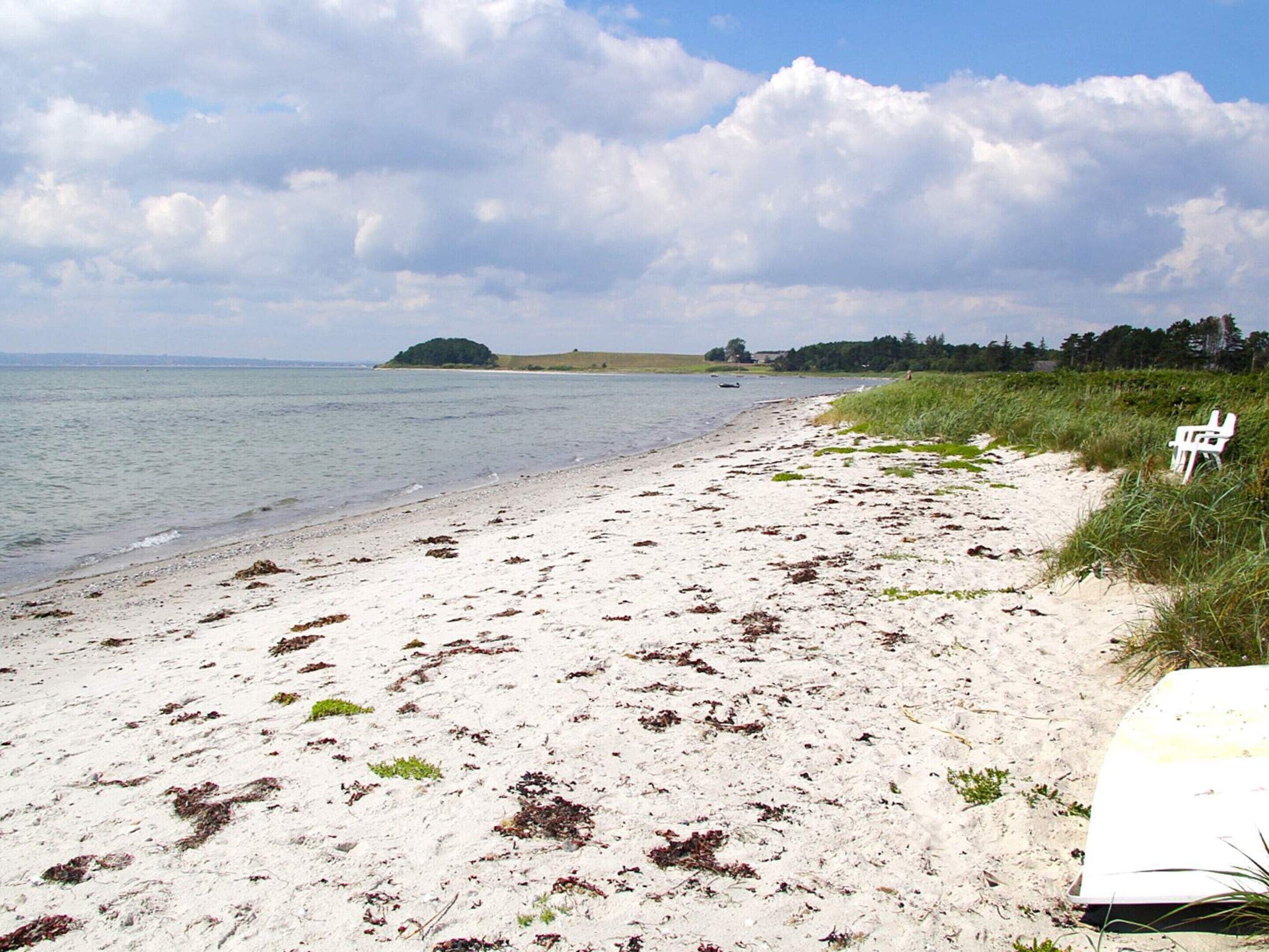 A beach with a white chair and a white object on the sand, a grassy area, and a body of water.