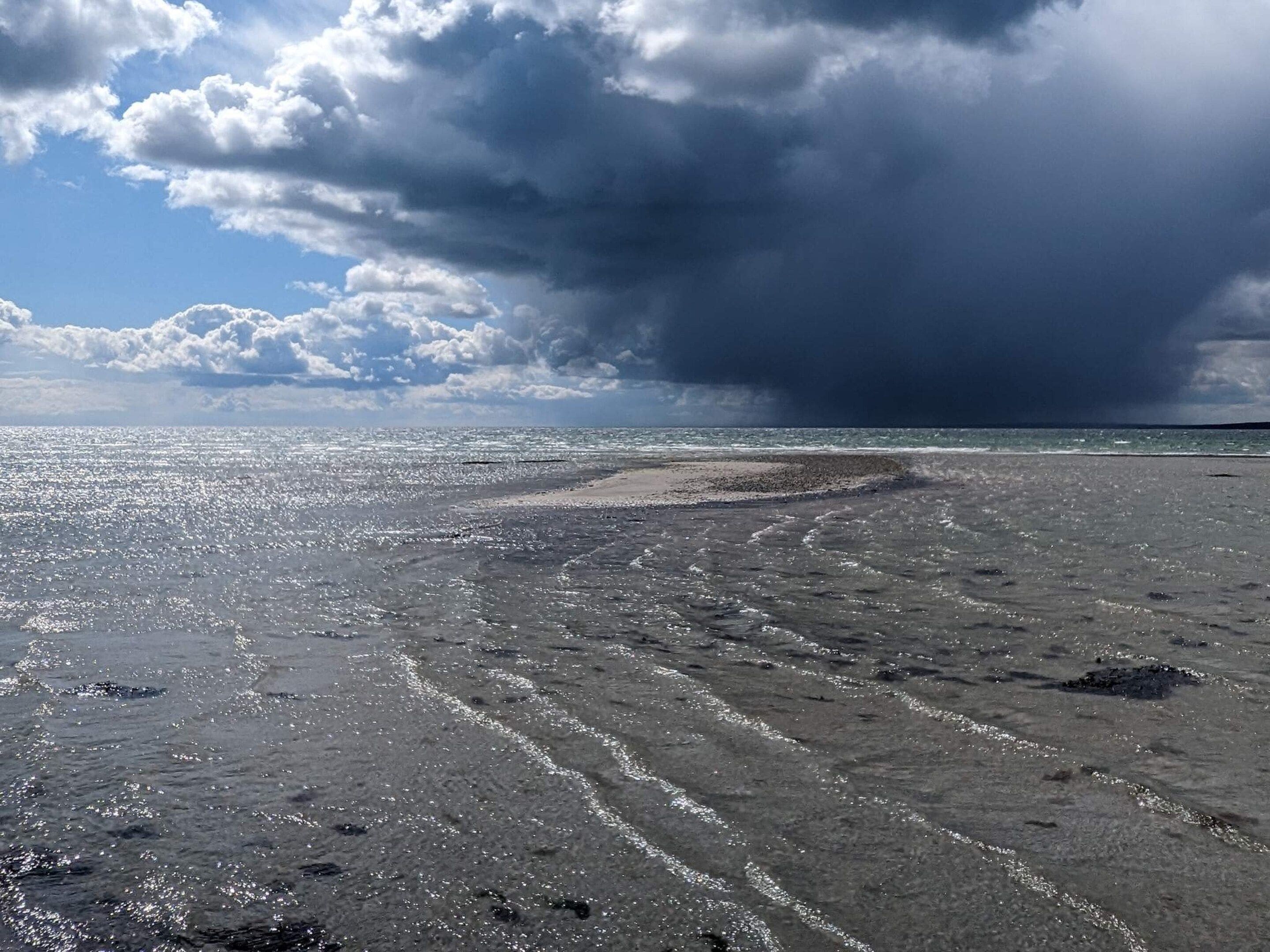 A beach with a curved shoreline, waves, and a partly cloudy sky.