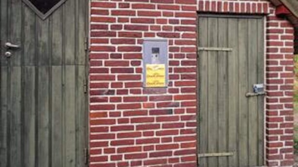 A brick wall with two wooden doors, one of which has a sign attached. - 6 Person Holiday Home in Norre Nebel (Norre Nebel)
