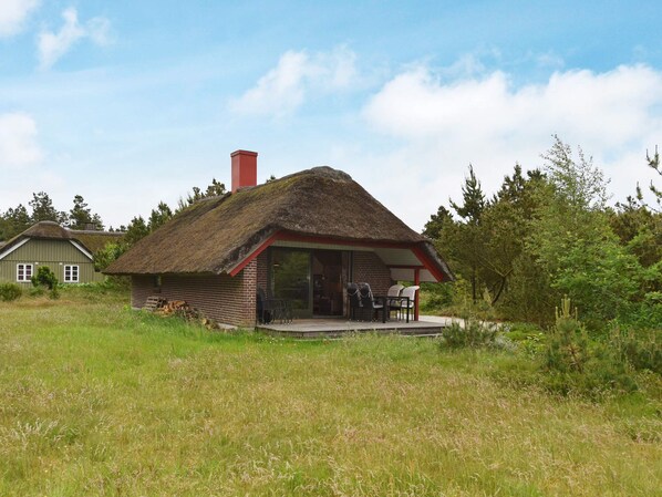 A thatched-roof house with a brick exterior, a chimney, and a porch with chairs.