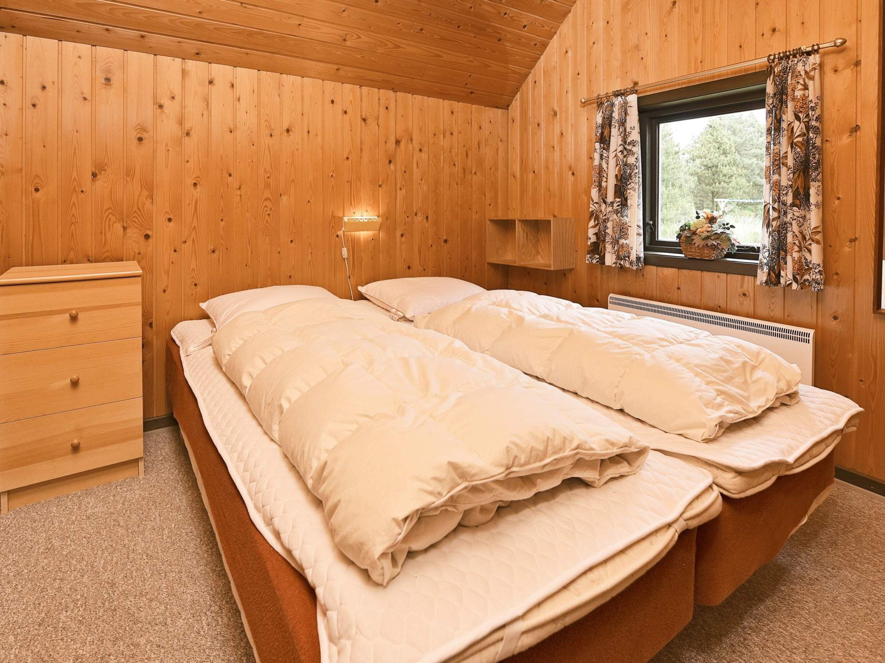 Quarto com painéis de madeira, cama, cômoda e janela com cortinas.