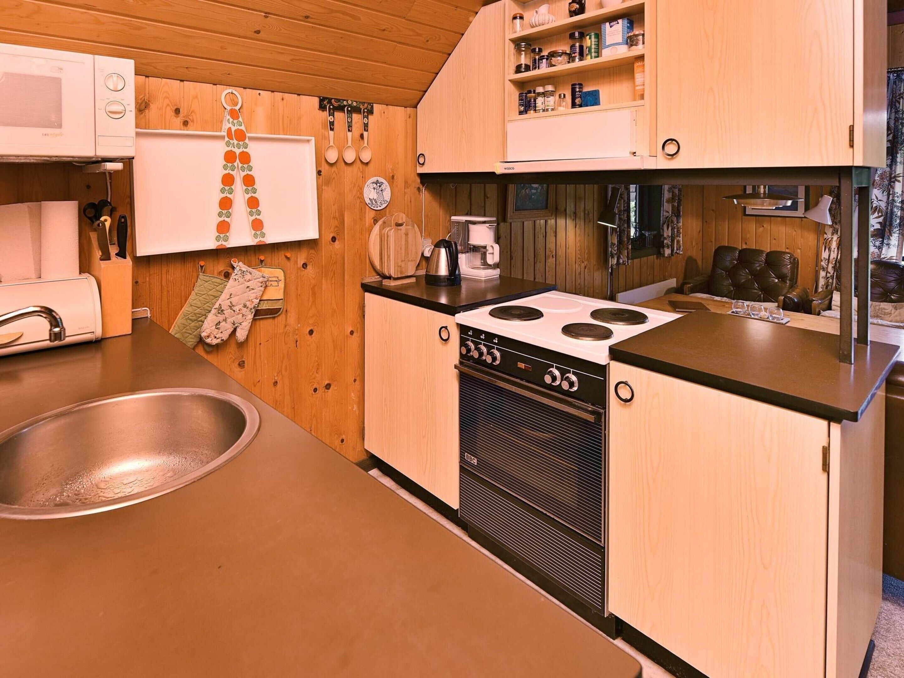 A compact kitchen with wooden cabinets, a stove, a sink, and a coffee maker.