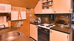 A compact kitchen with wooden cabinets, a stove, a sink, and a coffee maker. - 6 Person Holiday Home in Norre Nebel (Norre Nebel)