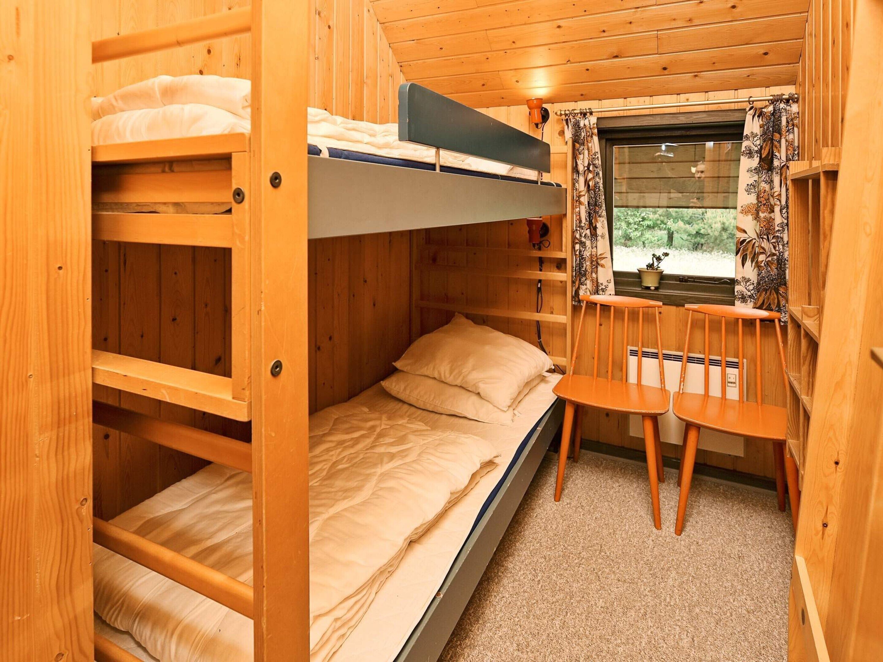 A bunk bed room with a window, a chair, and a small table.