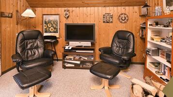 Una sala de estar acogedora con paredes de madera, dos sillones de cuero, un televisor, una estantería y una chimenea.