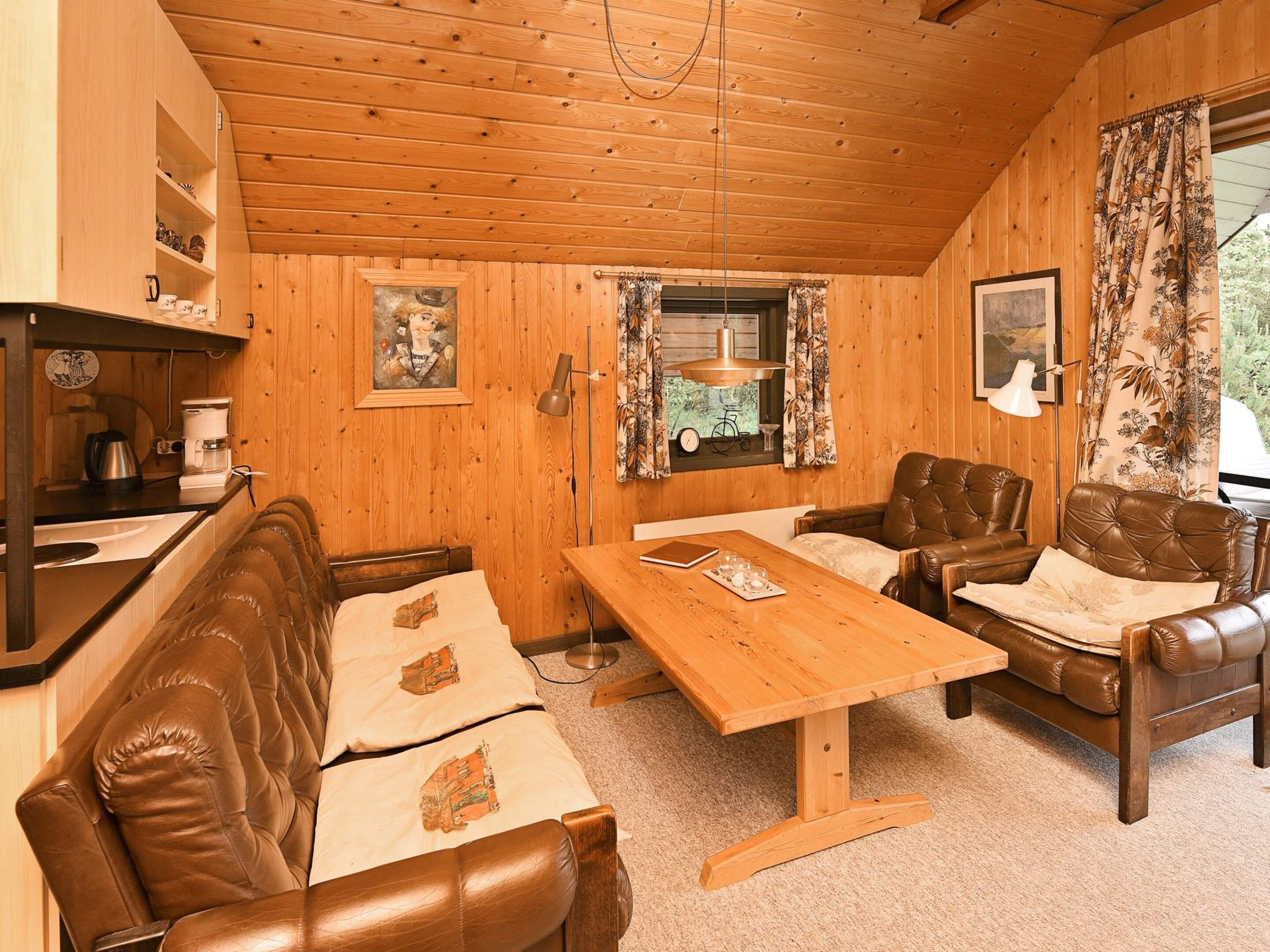 A cozy cabin interior with wooden walls, a dining table, leather sofas, and a small kitchen area.
