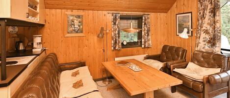 L’intérieur chaleureux d’un chalet avec des murs en bois, une table à manger, des canapés en cuir et un petit coin cuisine.