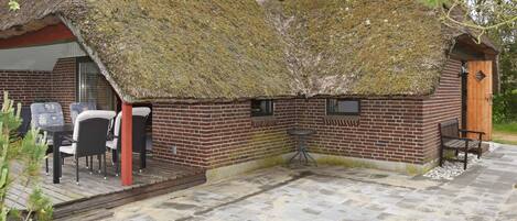 Ein reetgedecktes Cottage mit Backsteinfassade, einer kleinen Terrasse und Sitzgelegenheiten im Freien sowie einer Satellitenschüssel.