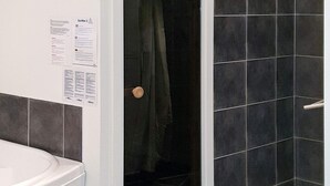 Ett badrum med en vit toalett, en duschhörna med mörka kakelplattor och en dörr med ett runt handtag.