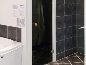 A bathroom with a white toilet, a shower area with dark tiles, and a door with a round handle. - 5 Star Holiday Home in Sydals (Sydals)