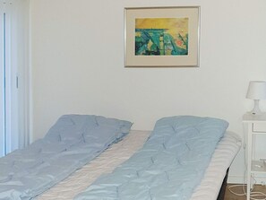 A single bed with a blue and white duvet, a bedside table with a lamp, and a framed painting on the wall. - 5 Star Holiday Home in Sydals (Sydals)