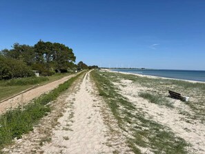 A sandy path leading to a beach with a bench and wind turbines in the distance. - 5 Star Holiday Home in Sydals (Sydals)