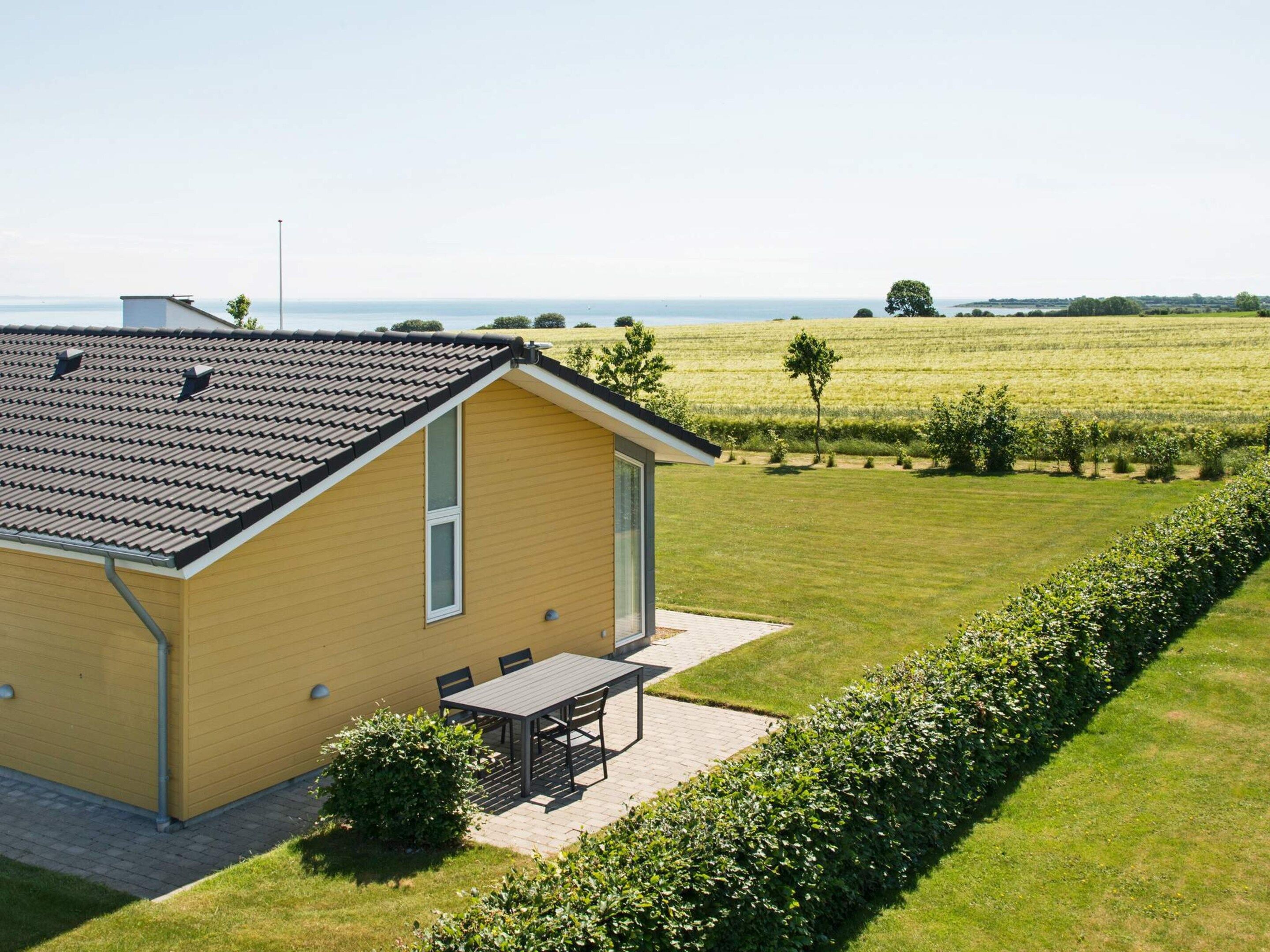 A single-story yellow building with a tiled roof, a patio with a table and chairs, and a well-maintained lawn.