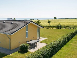 Un bâtiment jaune d’un seul étage, avec un toit en tuiles, une terrasse dotée d’une table et de chaises, et une pelouse bien entretenue.