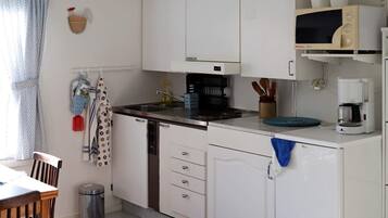 A compact kitchen with white cabinets, a microwave, a coffee maker, and a sink.