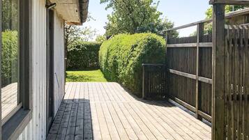 Una terraza de madera que conduce a una casa con fachada blanca y cerca negra.