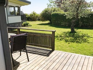 A deck with a chair and table, overlooking a well-maintained lawn and a tree with white blossoms.