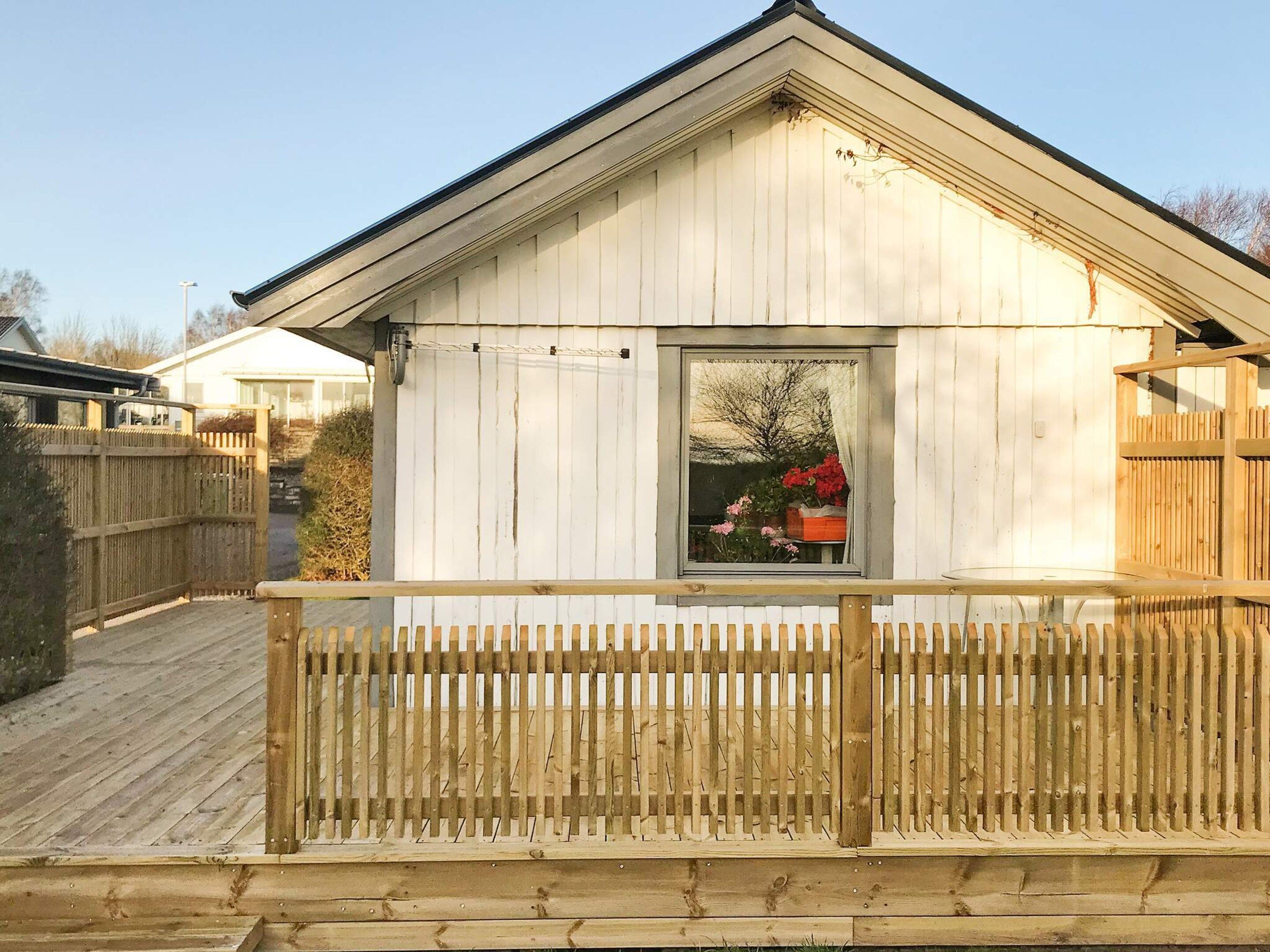 A wooden structure with a balcony, a window with a view of flowers, and a clear sky.