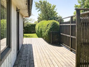 Une terrasse en bois mène à une maison à l’extérieur blanc et dotée d’une clôture noire.
