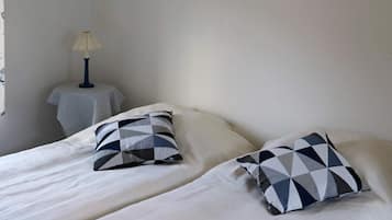 Un dormitorio con dos camas, cada una con un almohadón de diseño geométrico. Hay una pequeña mesa redonda con una lámpara junto a una de las camas.