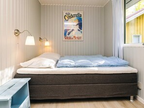 A neatly made bed with white and blue bedding, a dark brown bench, and a poster of 'Le Bal Royal Cindrella' on the wall.
