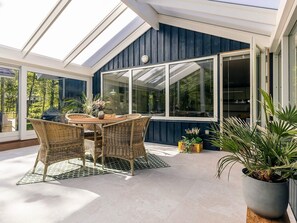 A sunlit patio with wicker furniture, a glass door leading inside, and potted plants.