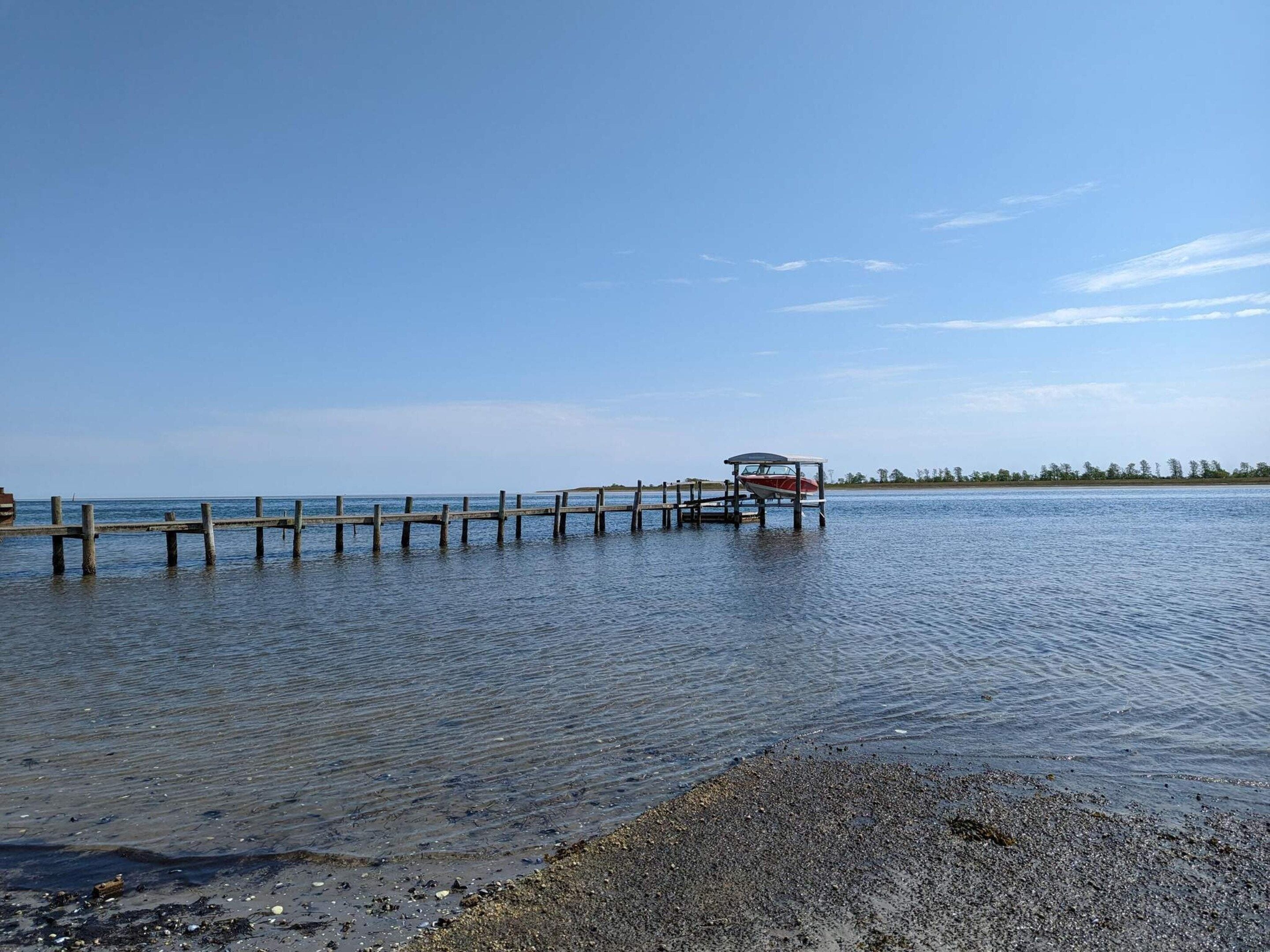 A wooden pier extending into calm water, a small boat docked at the end, and a distant shoreline with trees.