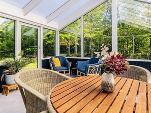 A conservatory with wicker furniture, a wooden table, and a vase of flowers.