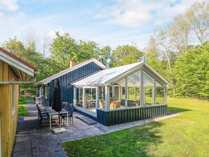 Ein Wintergarten mit Glasdach, eine Terrasse mit Tisch und Stühlen und Blick auf eine Rasenfläche.