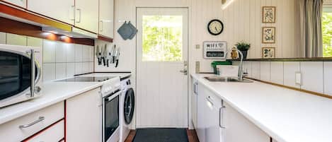 A compact kitchen with white cabinetry, a microwave, a stove, and a washing machine. There is a clock on the wall and a sign indicating WiFi password.