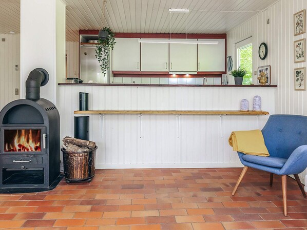 Una cocina acogedora con estufa de leña, armarios blancos y una silla azul.