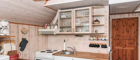 Cocina pequeña con muebles blancos, estufa y pileta.