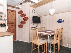 A room with a wooden wall, a television mounted on the wall, a clock, and a table with chairs. - 5 Person Holiday Home in Grindsted (Grindsted)