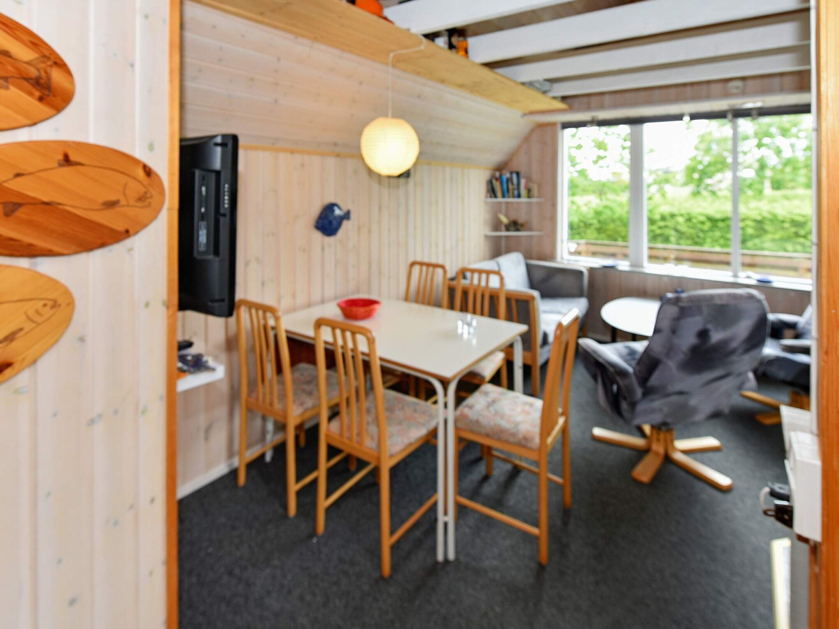 A dining area with a table and chairs, a television, and a view of greenery outside.