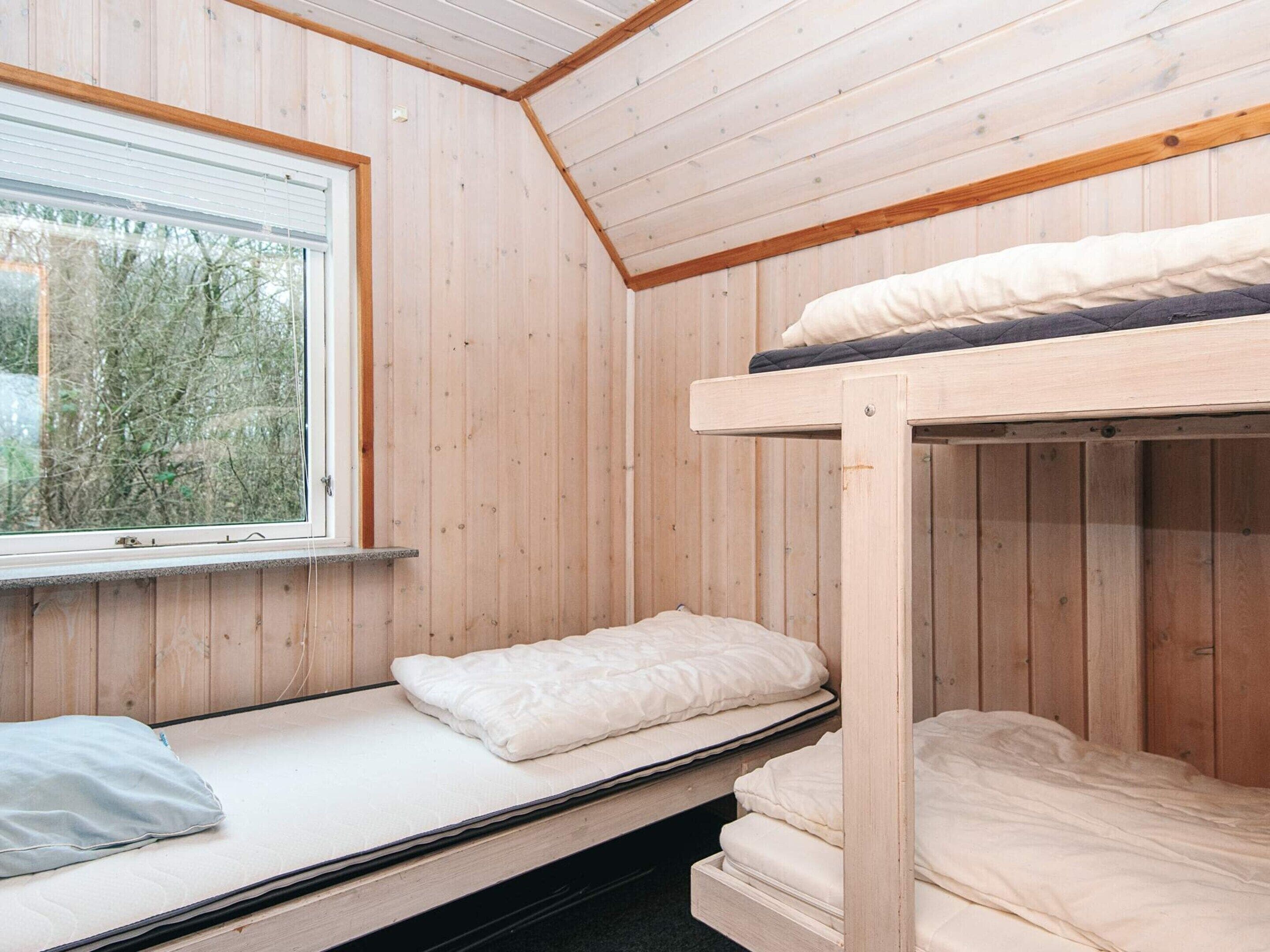 A room with wooden walls, a bunk bed, a window with blinds, and a view of trees outside.