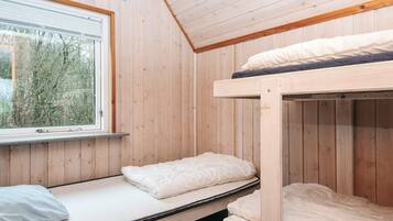 A room with wooden walls, a bunk bed, a window with blinds, and a view of trees outside.
