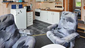 Cocina compacta con refrigerador, estufa y lavamanos. Hay dos sillas tapizadas y una mesita.