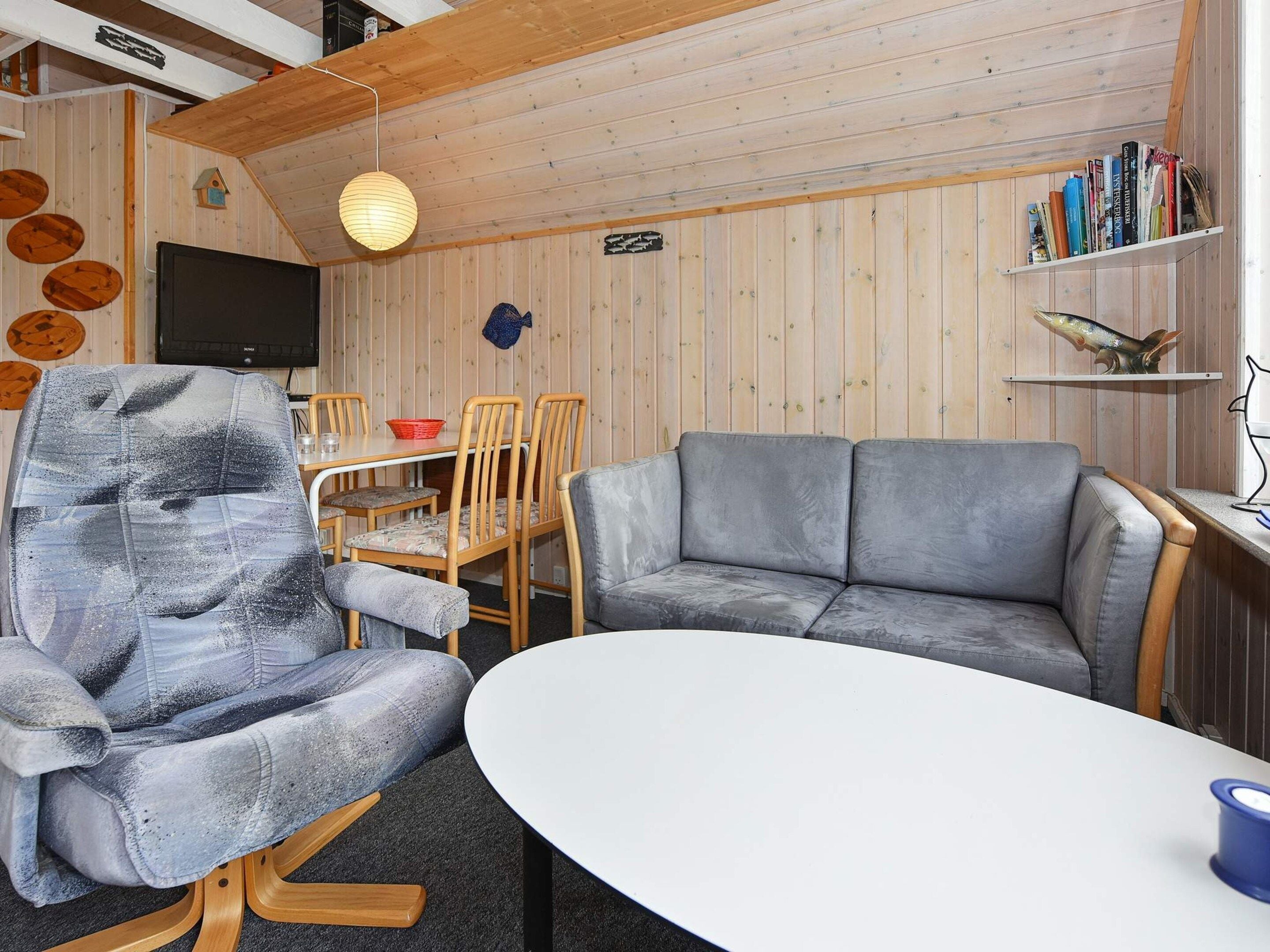 A cozy room with a grey sofa, a round table, a television, and a bookshelf with books and a fish decoration.