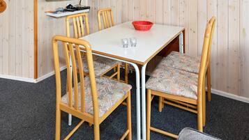 A dining area with a white table, four wooden chairs with patterned cushions, and a red bowl on the table.