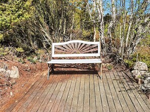 A wooden bench with a sunburst design, situated on a wooden deck surrounded by dense shrubbery.
