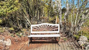 A wooden bench with a sunburst design, located on a wooden deck surrounded by natural vegetation.